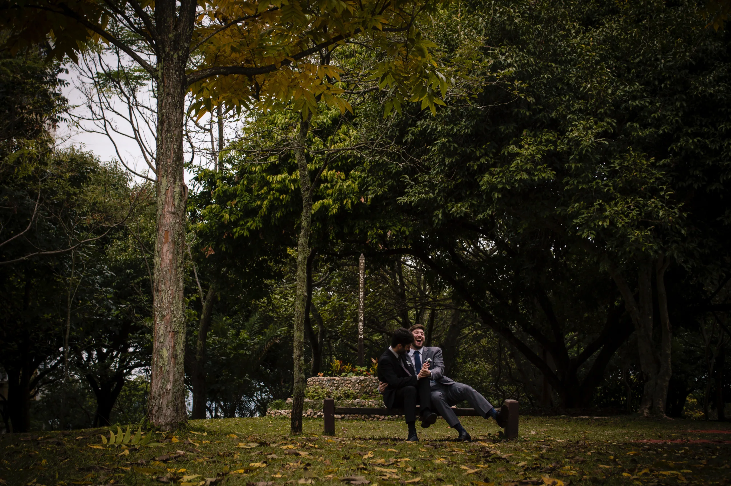 man in black jacket sitting on brown wooden bench near green trees during daytime